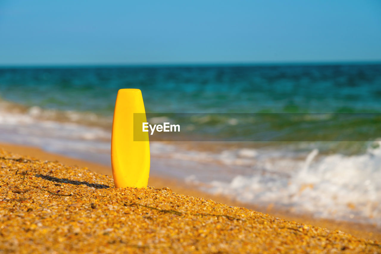 A bottle of sunscreen without a label on the beach on a sunny day. blank for advertising your cream