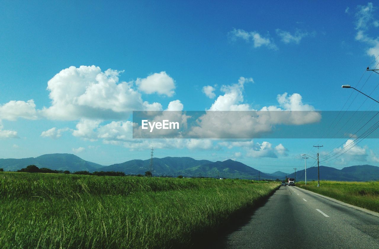 Road amidst grassy landscape against blue sky