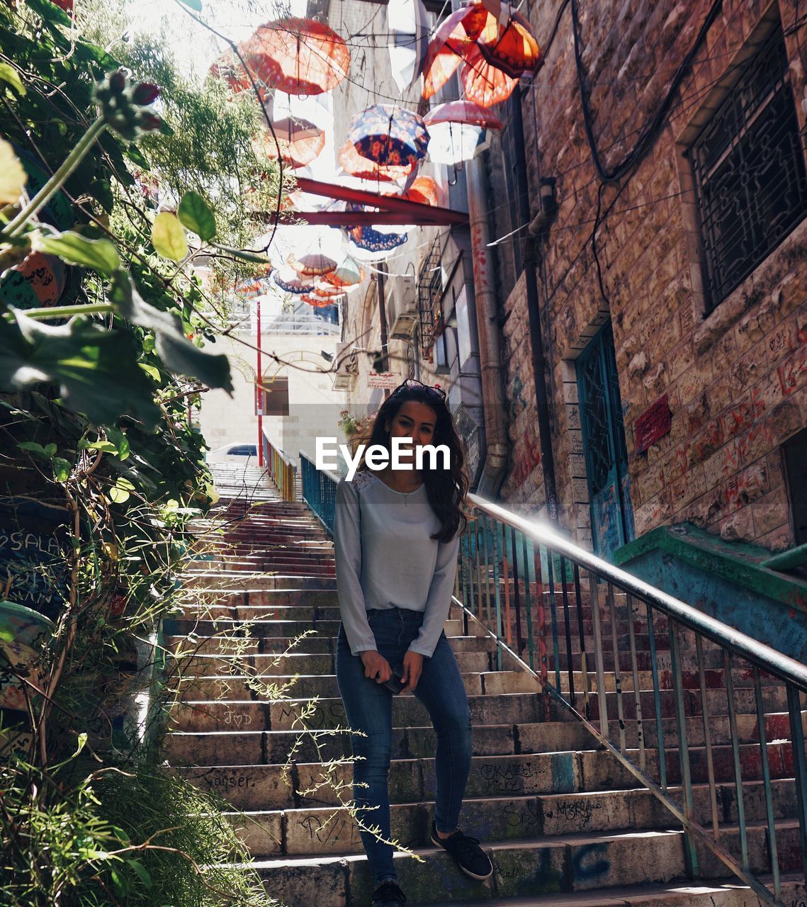 PORTRAIT OF YOUNG WOMAN ON STAIRCASE AGAINST BUILDINGS