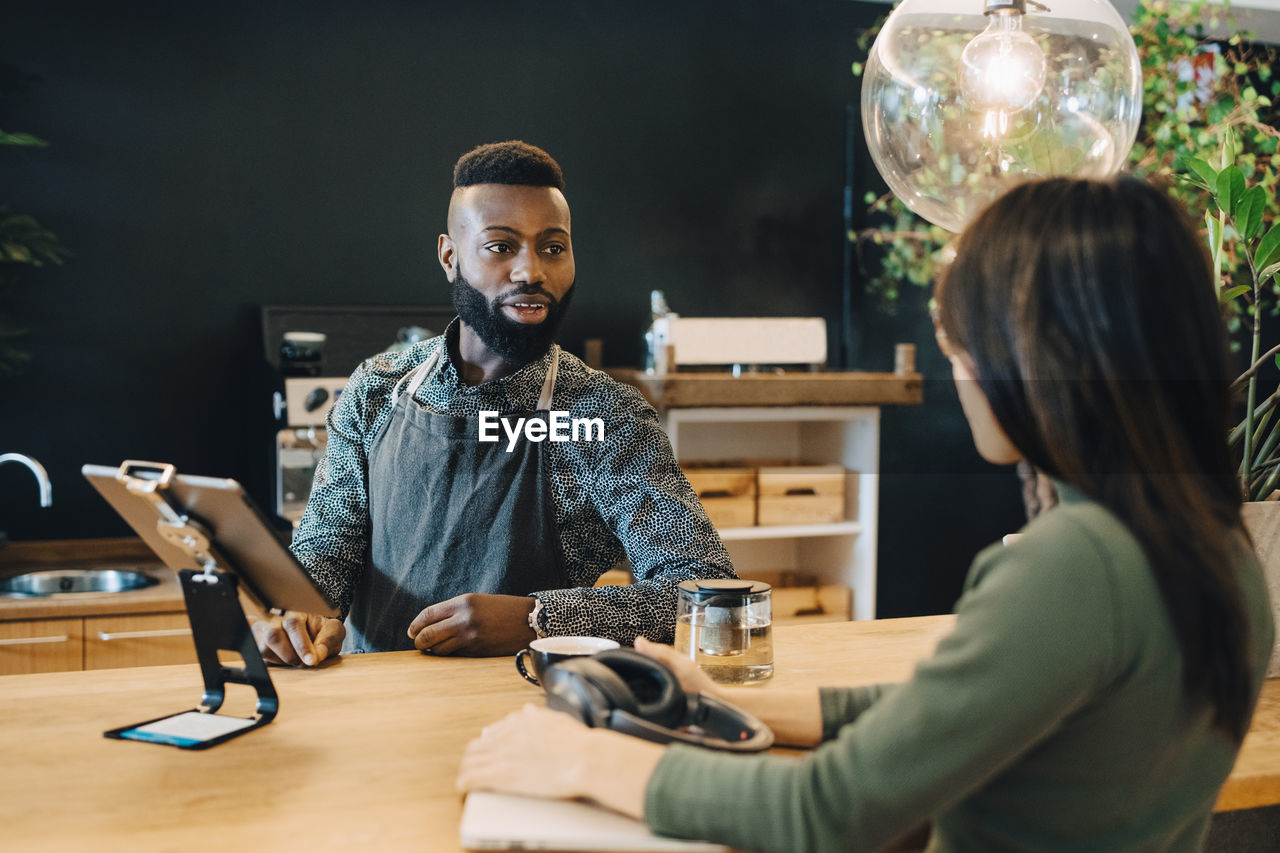 Male owner talking with female customer at coffee shop