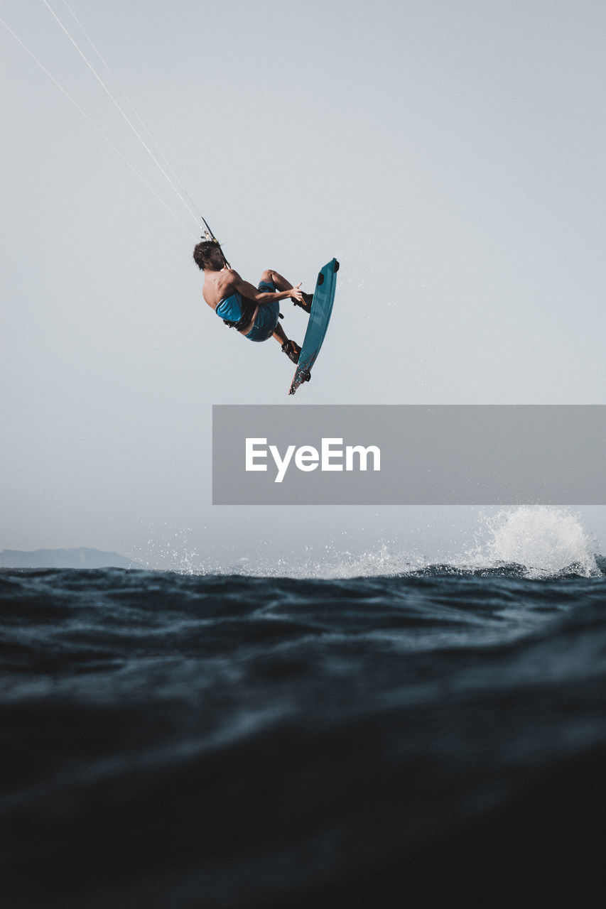 Side view of man kiteboarding in sea against clear sky