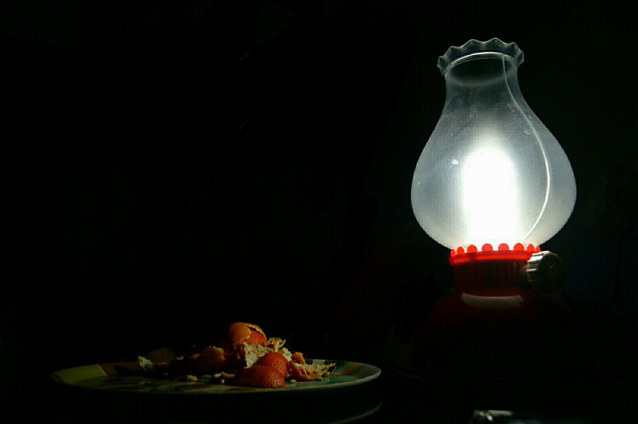 Close-up of peeled oranges in plate by illuminated lantern against black background