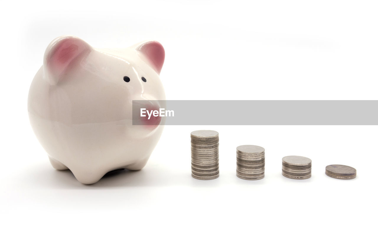 Close-up of coins with piggy bank on white background