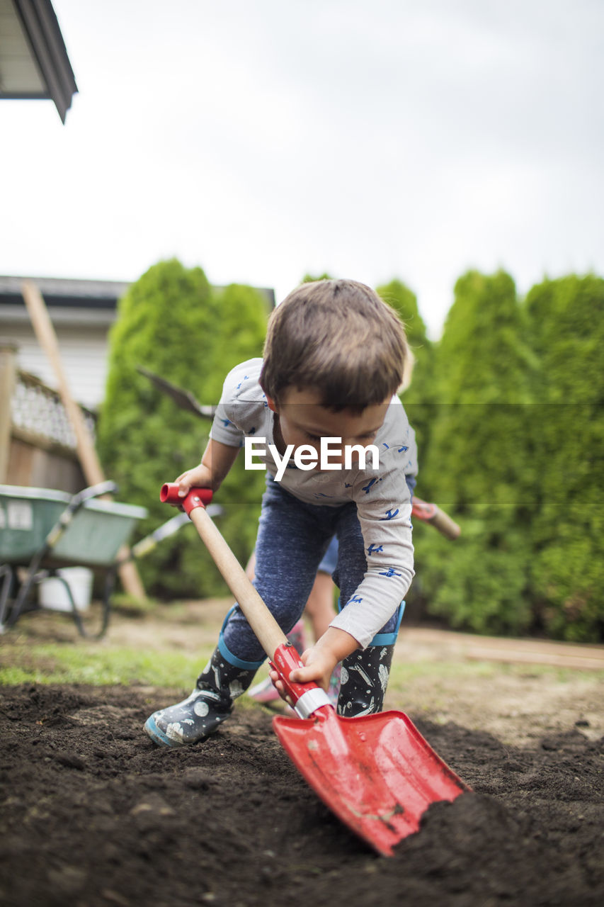 Handsome strong young man shoveling soil in backyard.