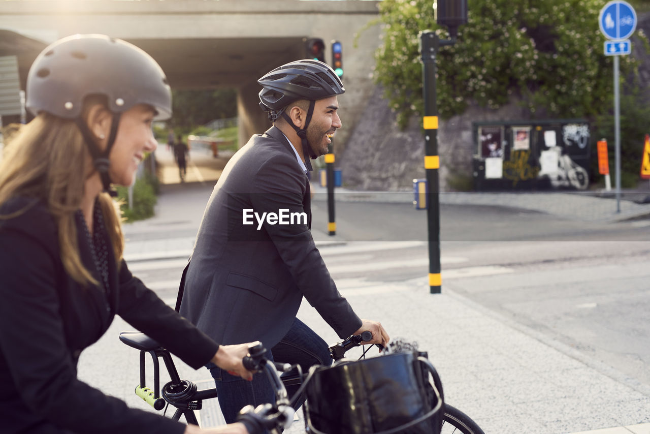 Side view of smiling business coworkers cycling in city