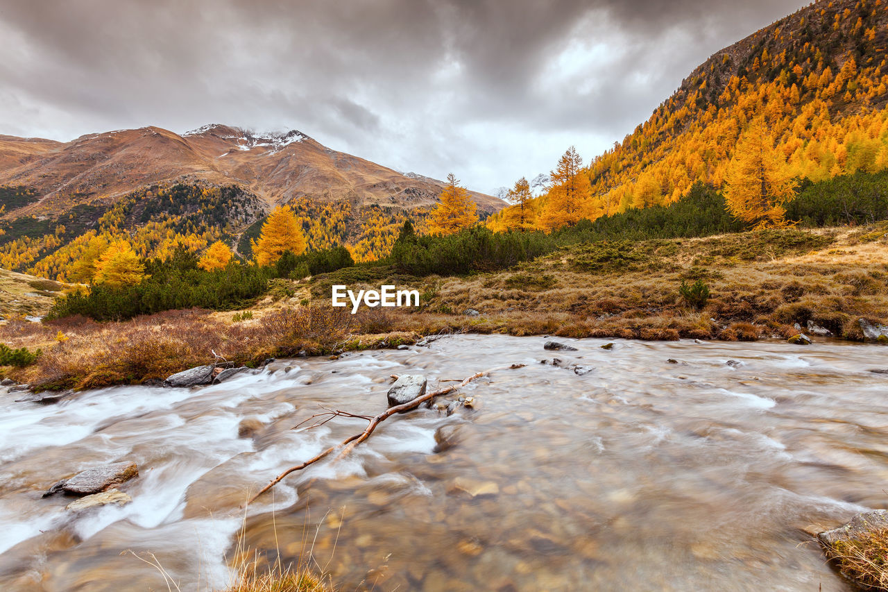 SCENIC VIEW OF RIVER FLOWING BY MOUNTAINS AGAINST SKY