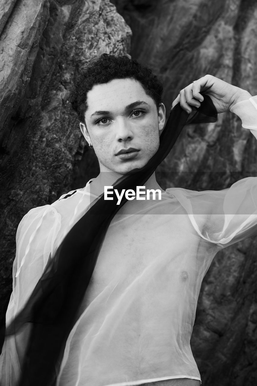 Young male with  androgynous look shot outdoor in black and white with rocks in background.