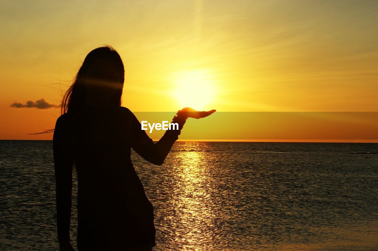 Optical illusion of woman holding sun during sunset
