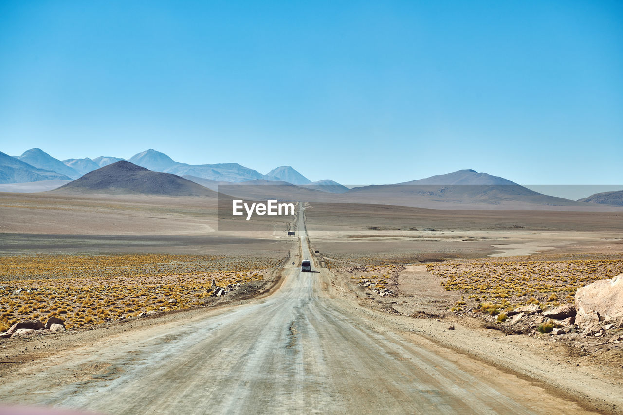 Road leading towards desert against clear sky