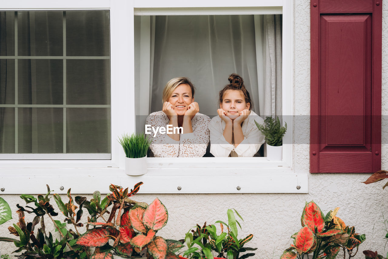 Portrait of woman and girl sitting on window