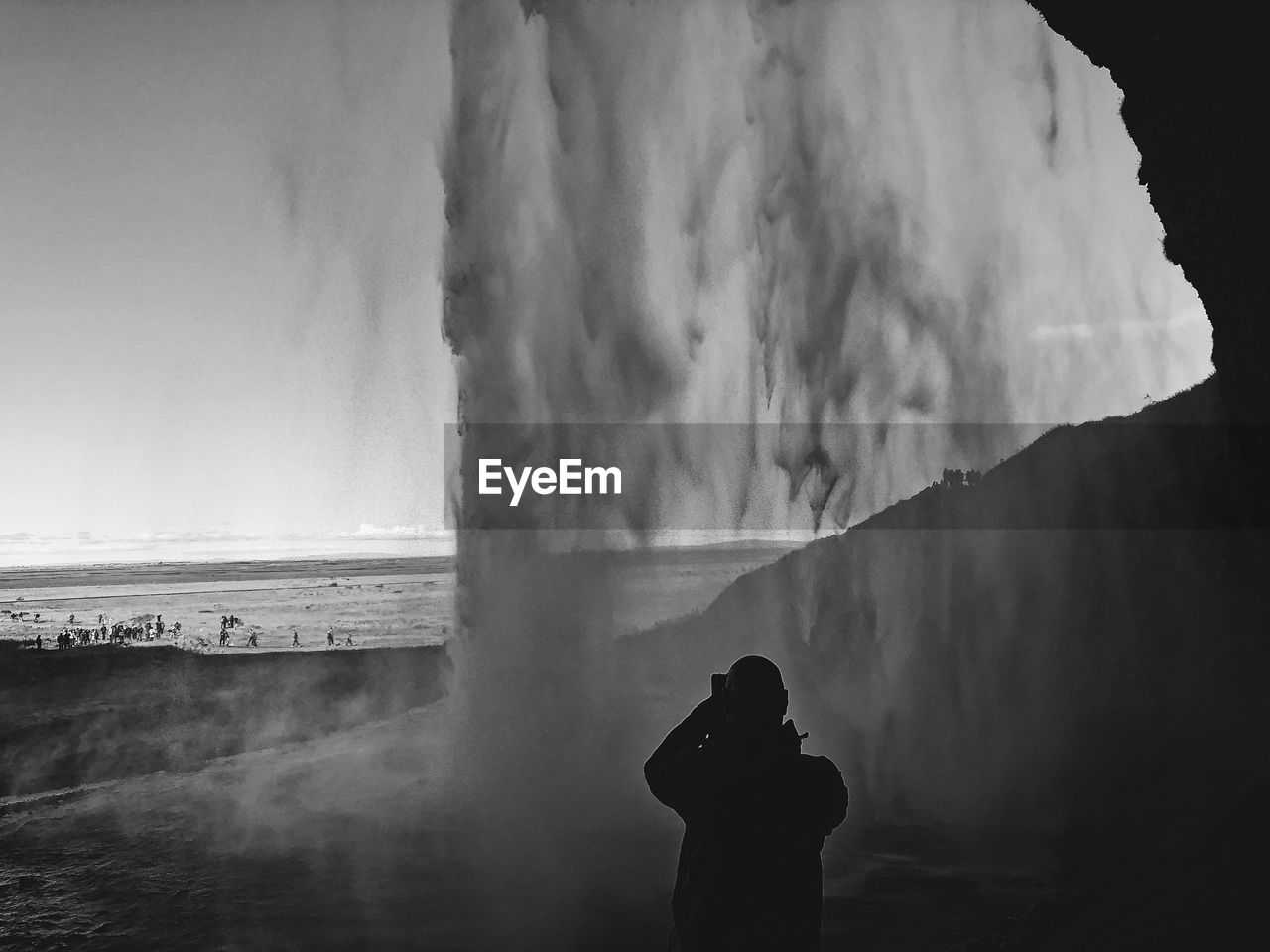 Rear view of silhouette man standing by waterfall against sky