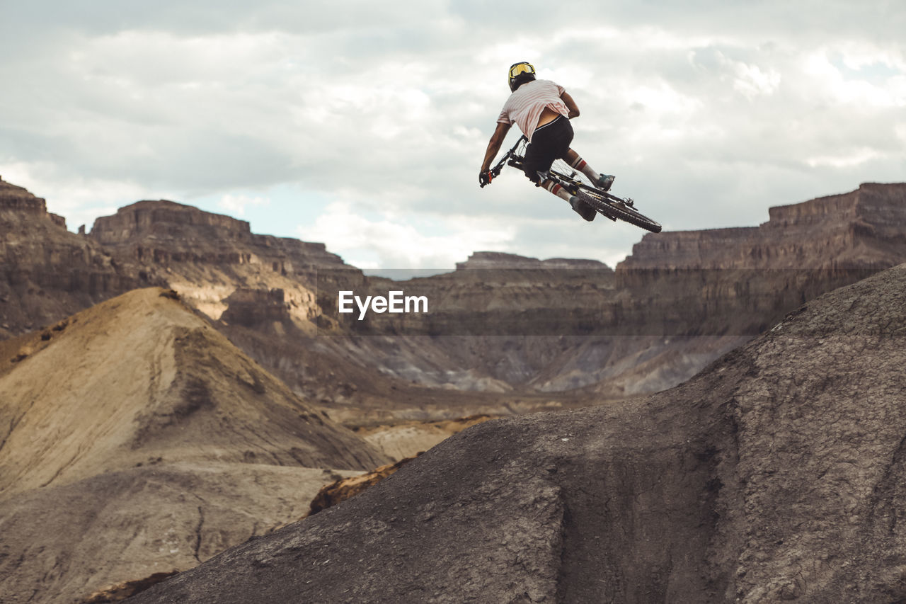 Rear view of young male jumping with mountain bike in desert landscape