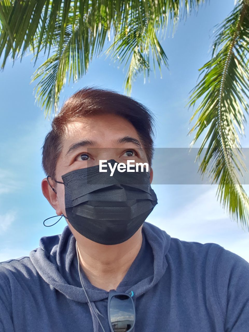 Portrait of young man with palm trees against sky