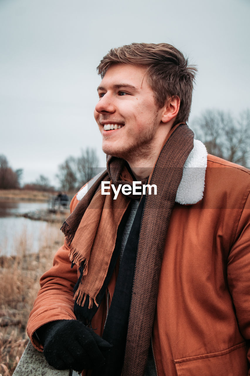 Smiling young man looking away while standing against sky