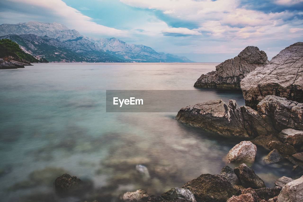 Rocks in river by mountains against sky