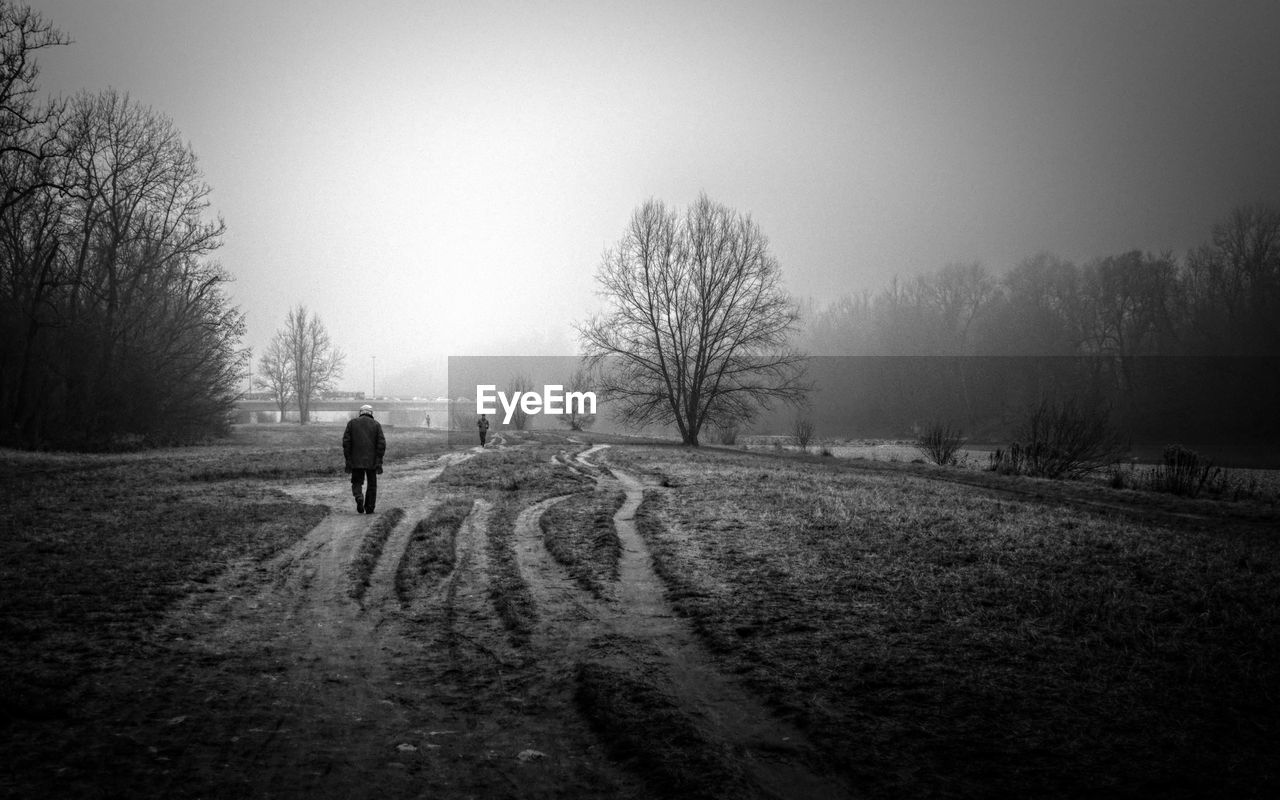 MAN WALKING ON SNOW FIELD AGAINST SKY