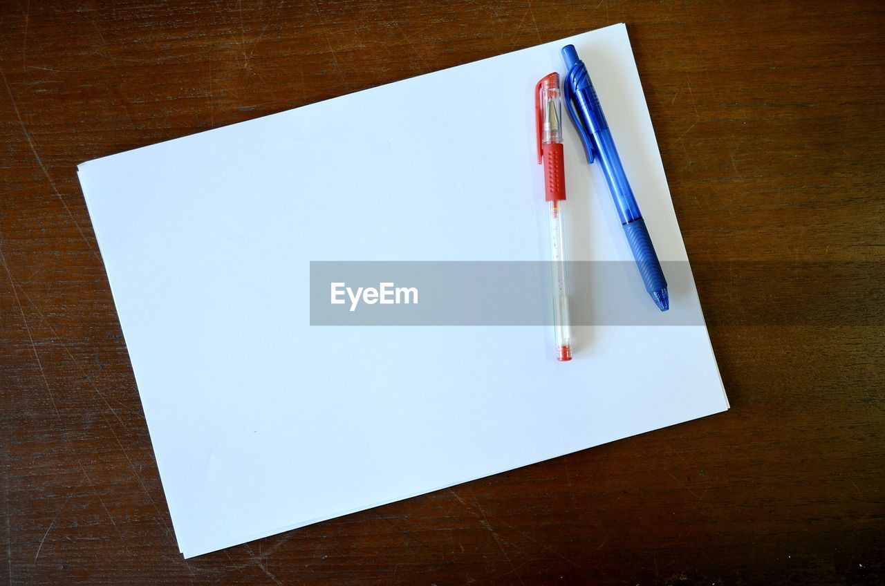 High angle view of pens with blank paper on wooden table