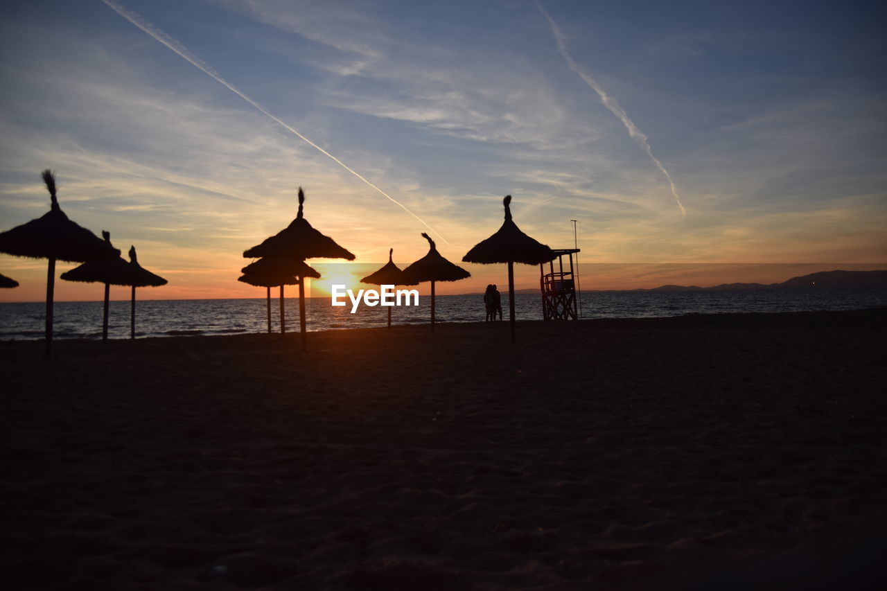 SILHOUETTE PARASOLS ON BEACH AGAINST SKY AT SUNSET