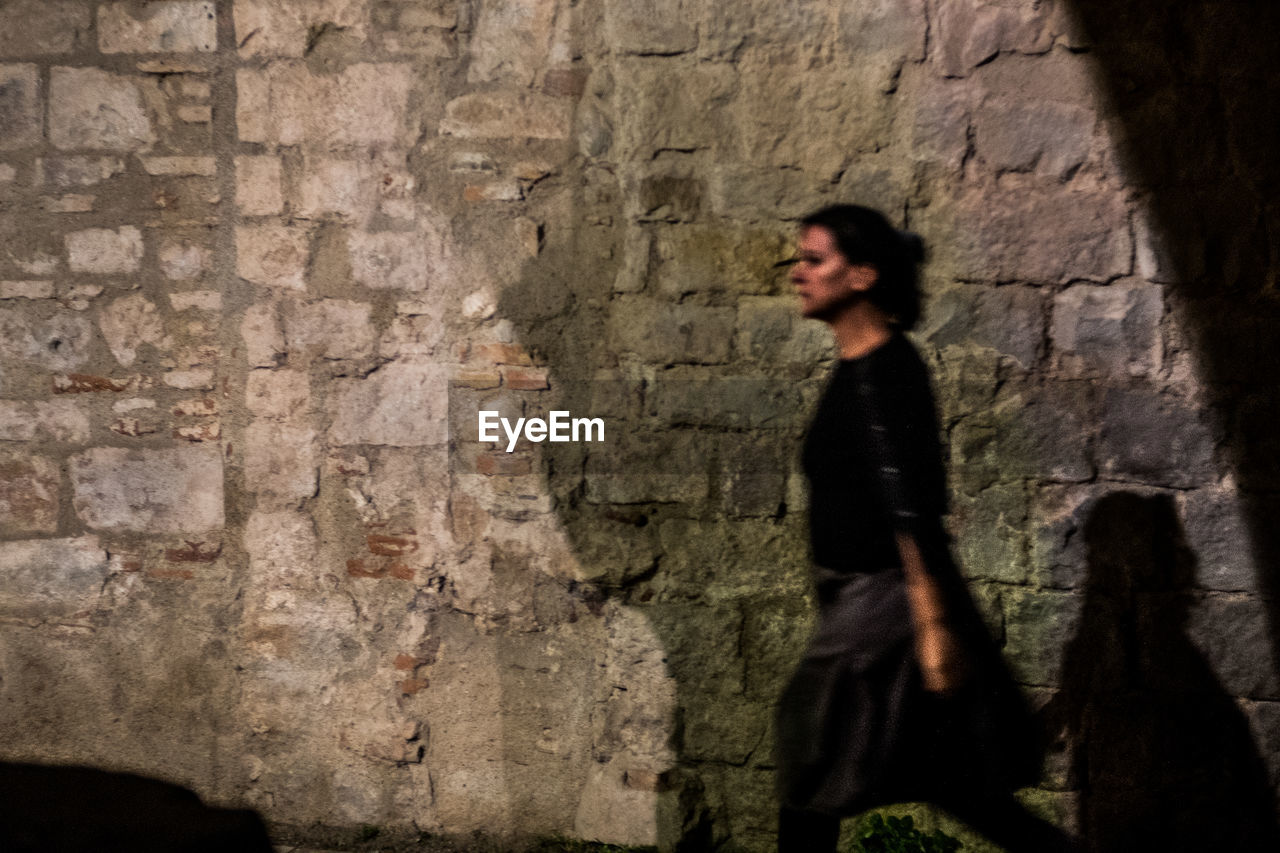 YOUNG WOMAN STANDING AGAINST WALL