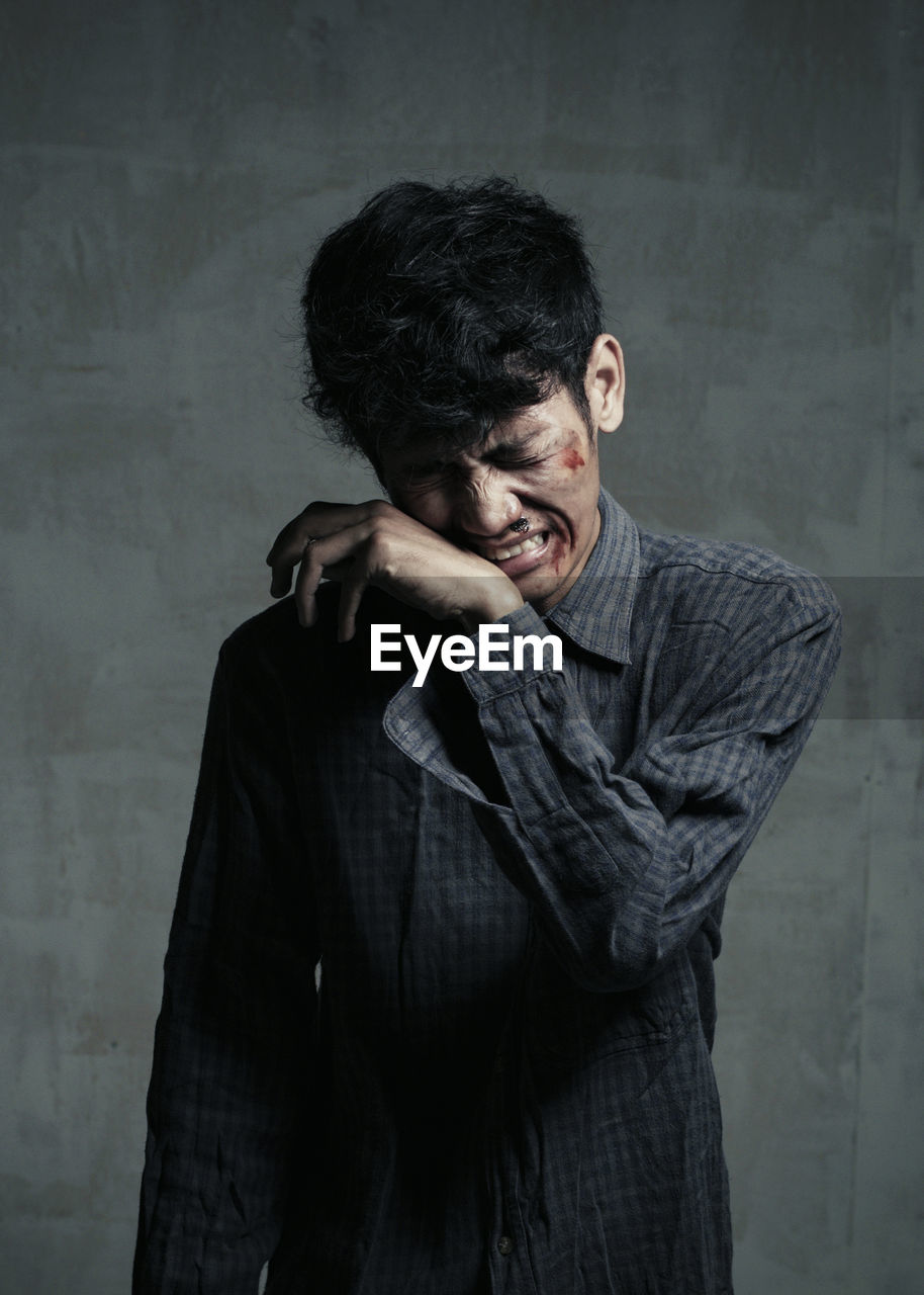 Injured young man crying while standing against wall