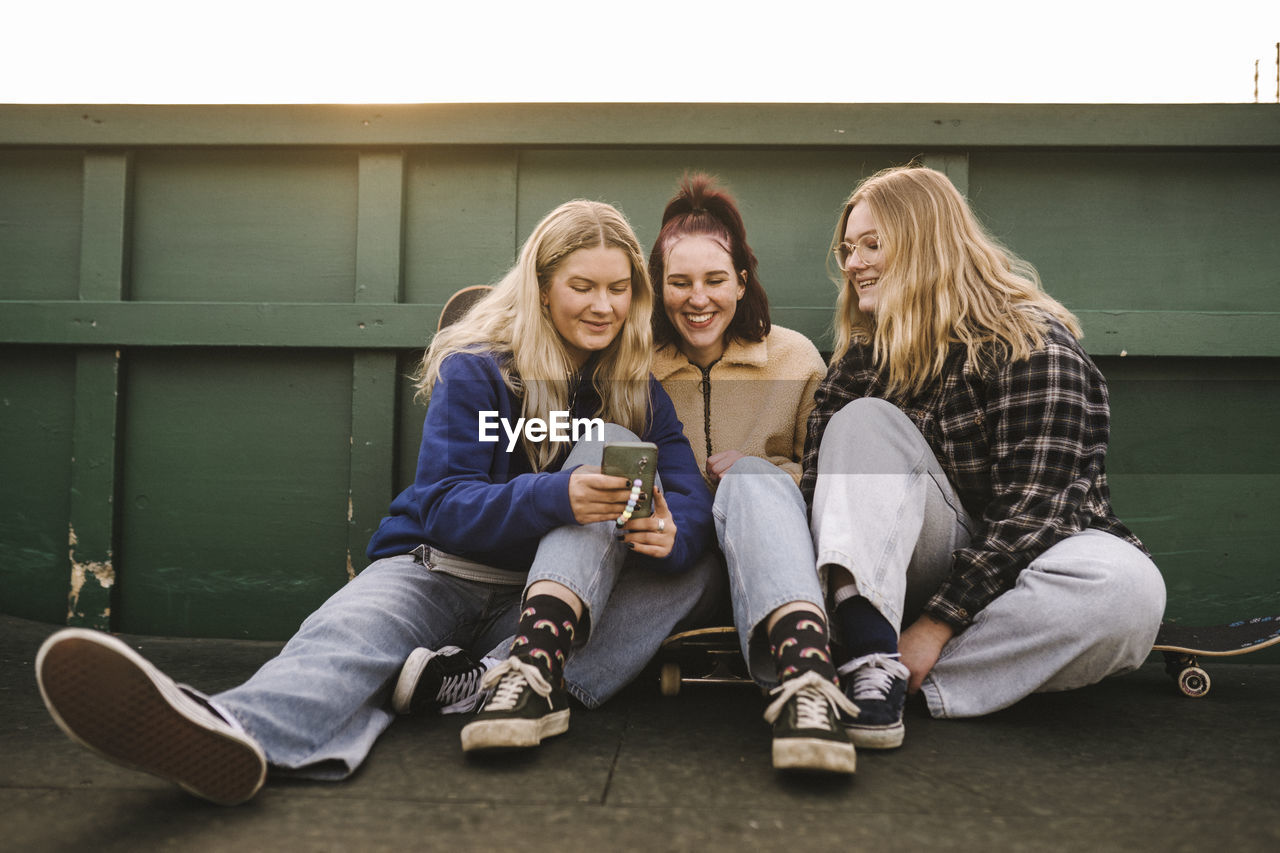 Teenage girls sitting on skateboards and using smart phone