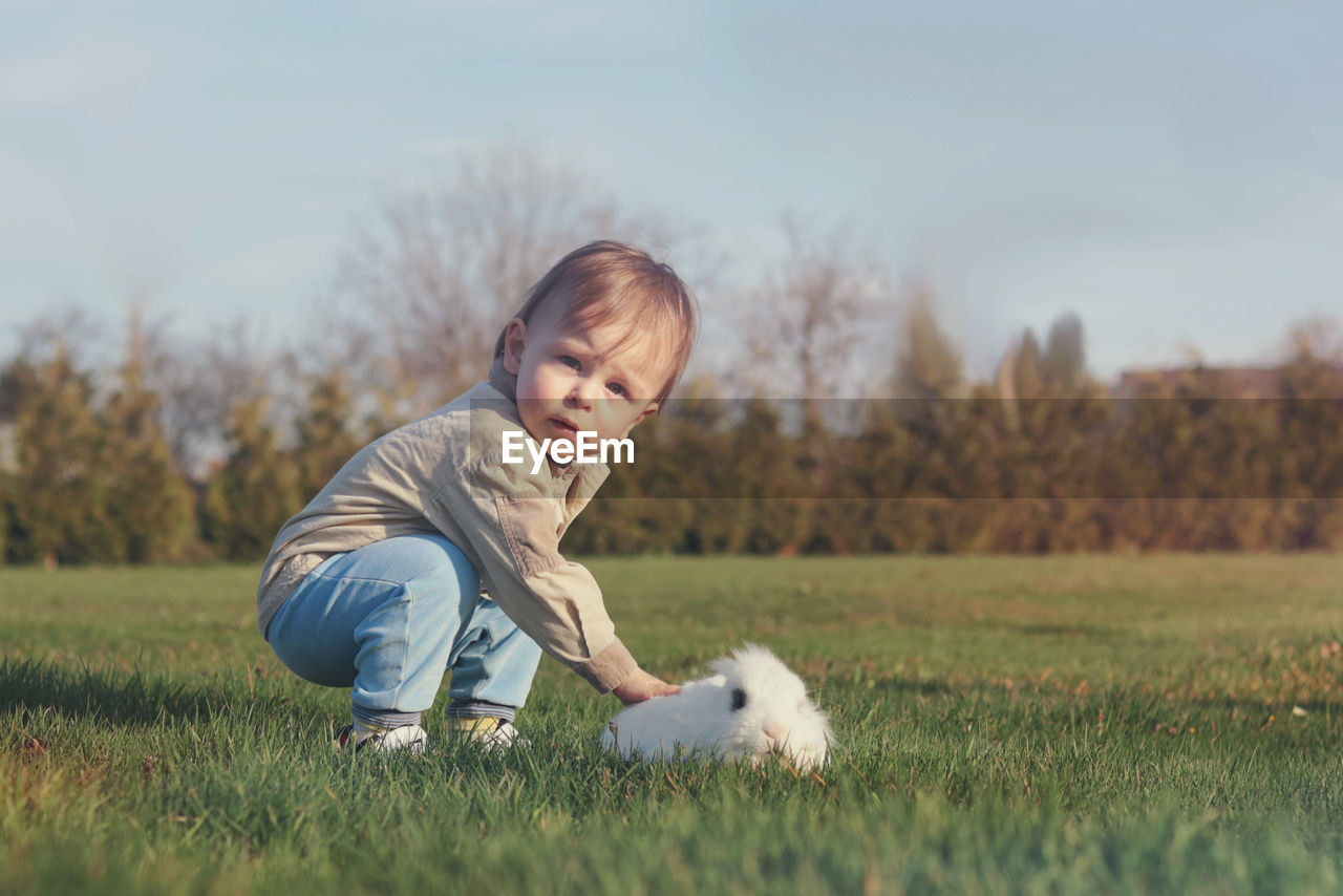 Cute baby boy and white fluffy bunny in the garden 