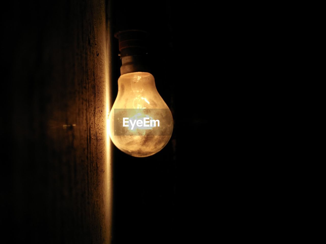 CLOSE-UP OF LIGHT BULB HANGING ON BLACK BACKGROUND