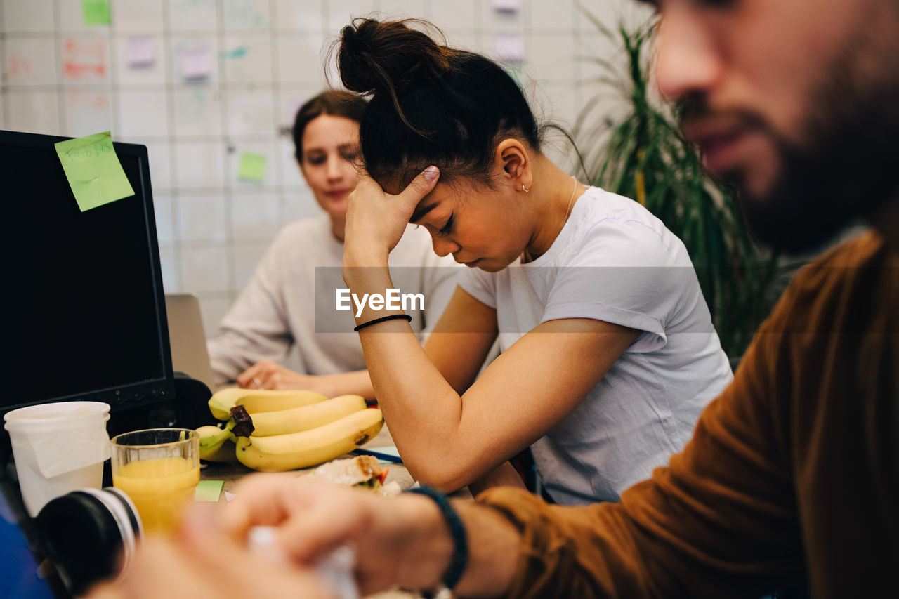 Worried businesswoman sitting amidst colleagues at desk in creative office