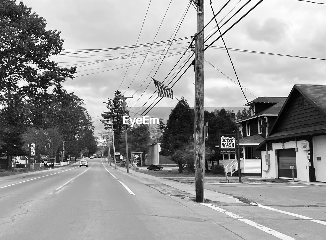 road, street, transportation, architecture, cable, residential area, lane, sky, electricity, tree, city, infrastructure, black and white, built structure, building exterior, monochrome, nature, cloud, power line, sign, neighbourhood, monochrome photography, plant, the way forward, suburb, mode of transportation, technology, electricity pylon, urban area, day, no people, car, house, building, symbol, road marking, motor vehicle, power generation, outdoors, power supply, marking, diminishing perspective, residential district, white, vanishing point, road surface, black, town, city street, communication, transport, travel destinations
