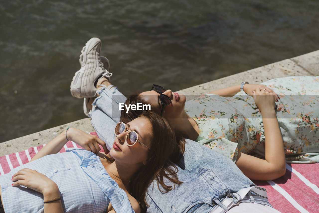 Female friends relaxing on lap of man by river