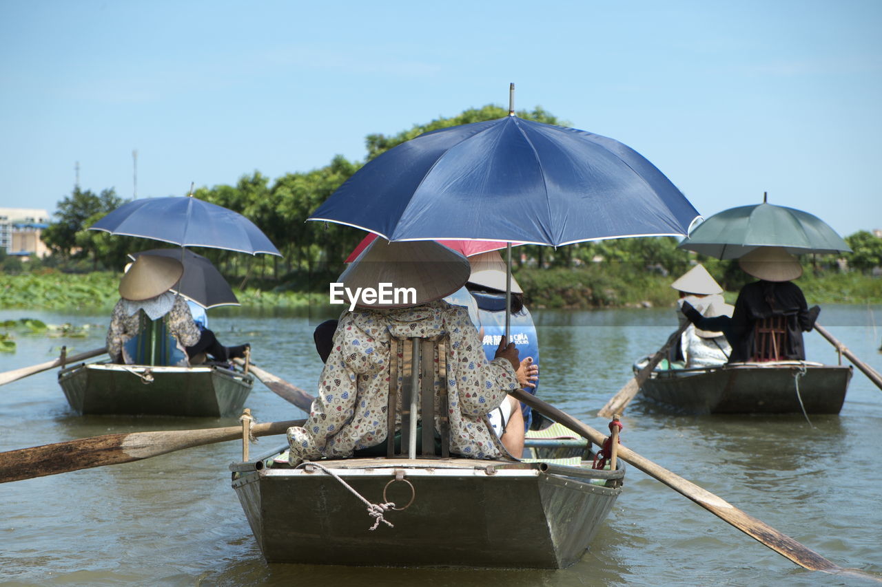 People on boat carrying umbrellas while rowing in lake