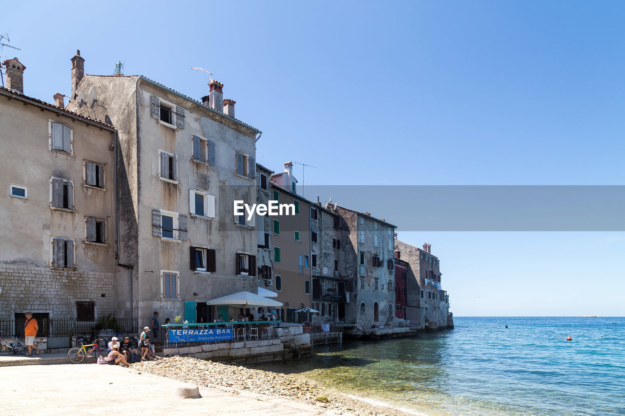 Buildings by sea against clear blue sky