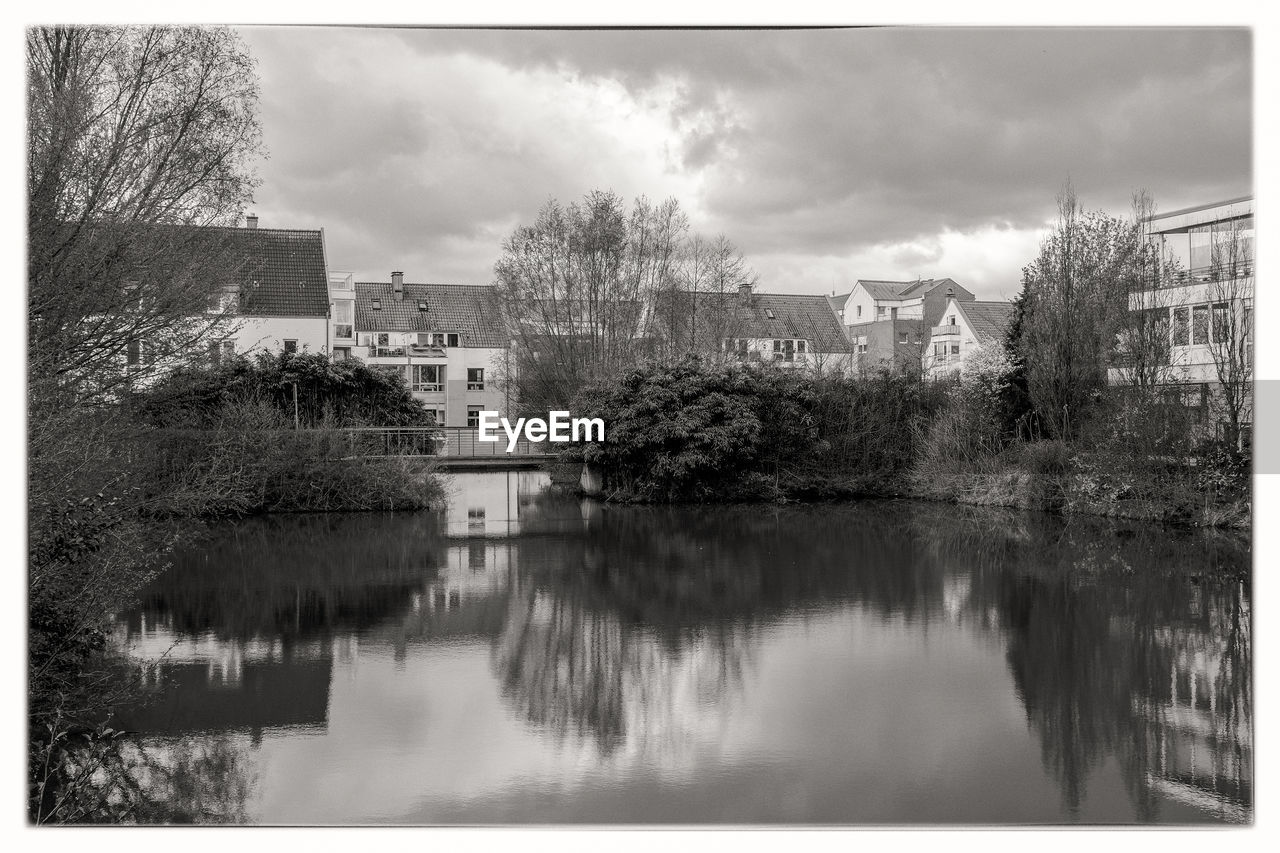 Lake by houses in town against sky