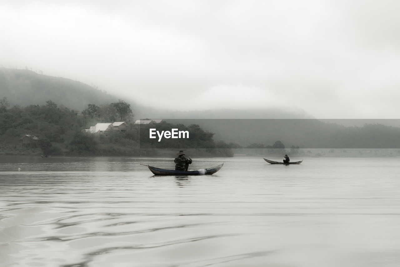 PEOPLE ON BOAT IN LAKE AGAINST SKY