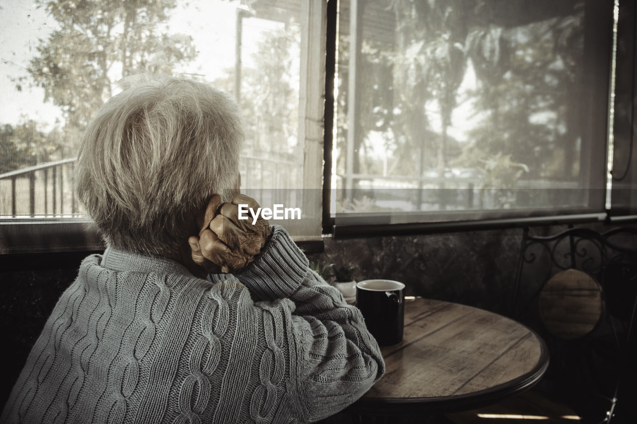 Rear view of old person sitting by window at home. concept loneliness, dementia, abuse, sadness.