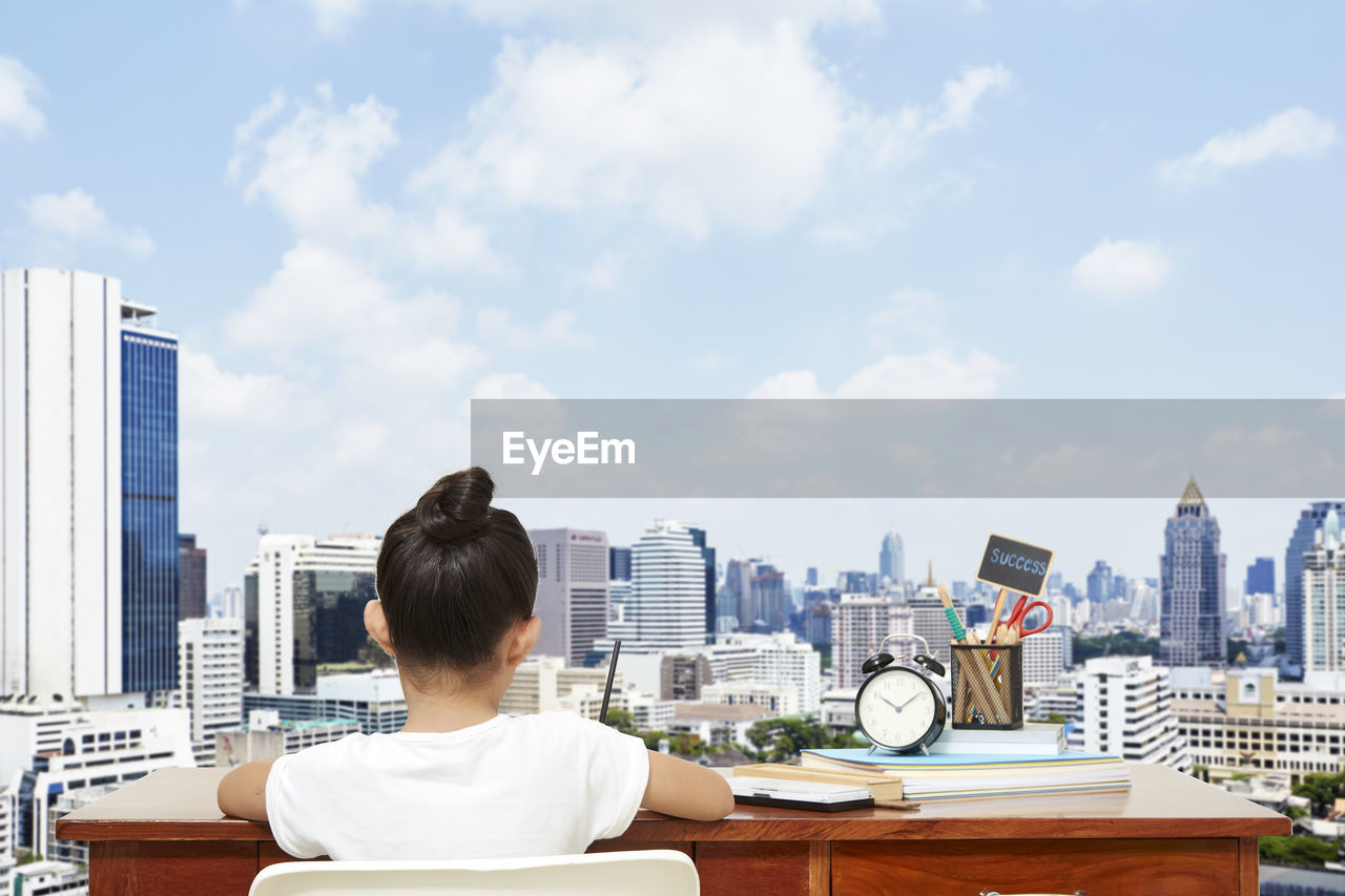 Digital composite image of girl studying against buildings