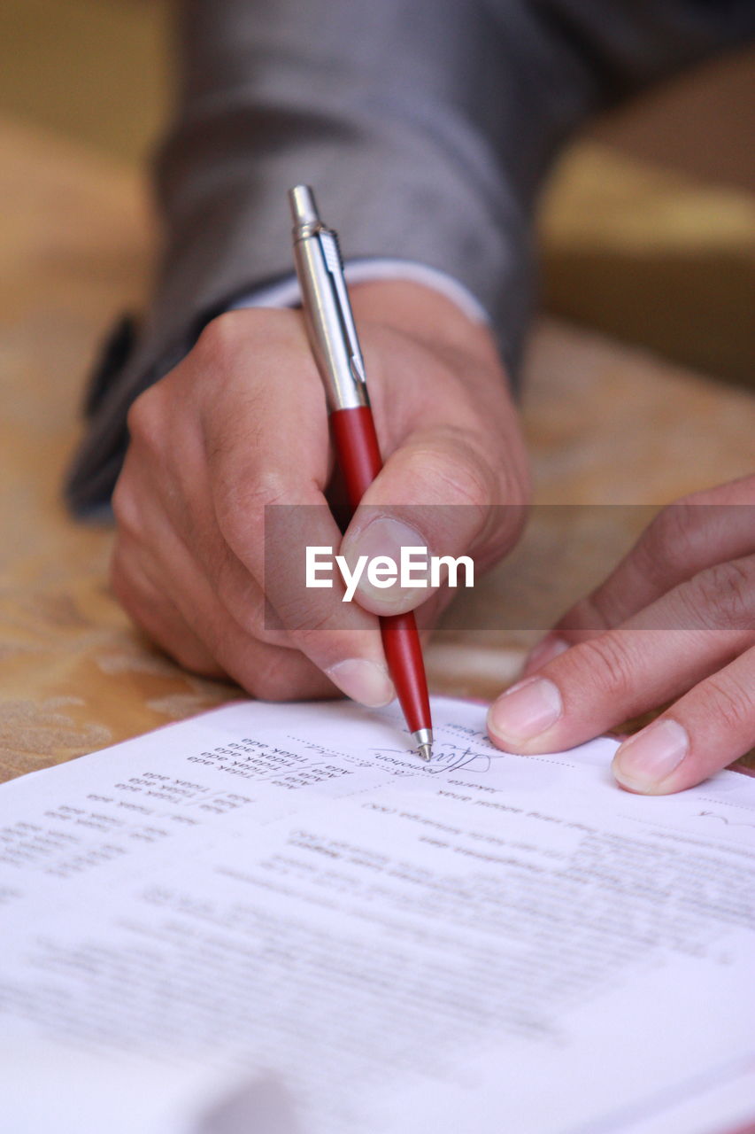 Cropped hands of man signing over papers on table