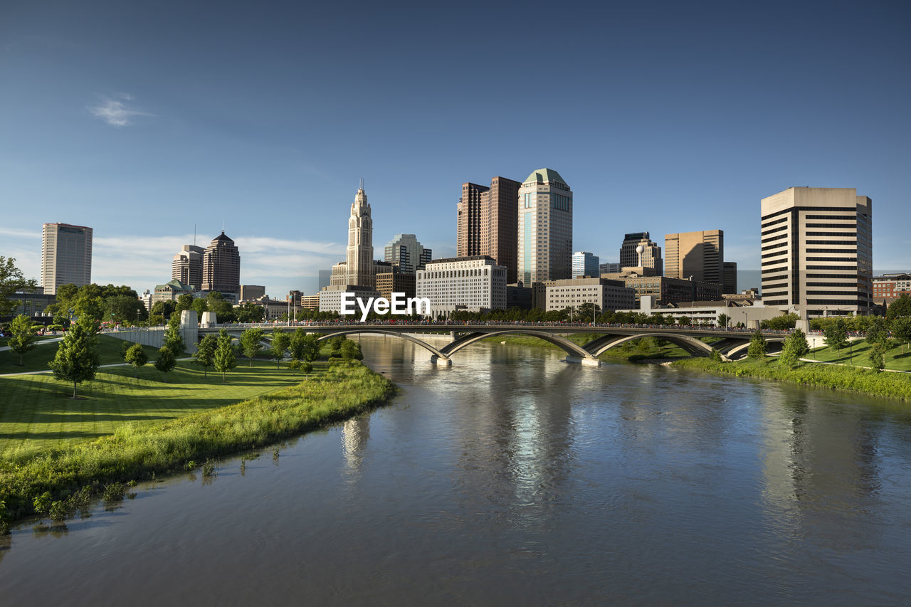 Bridge over river by buildings in city against blue sky