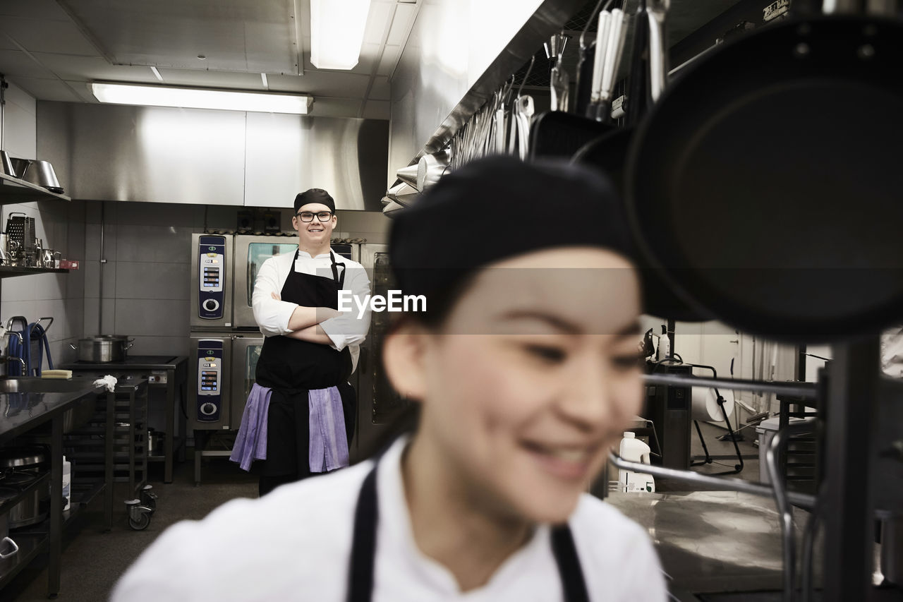 Portrait of confident male chef with colleague in foreground at commercial kitchen