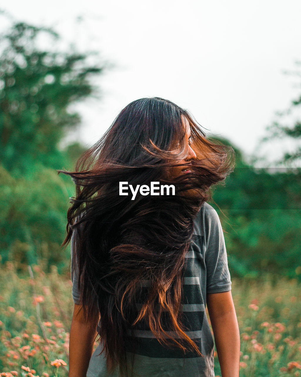 Woman flipping hairs while standing against trees