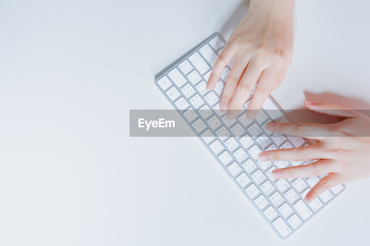 Cropped hands typing on keyboard against white background