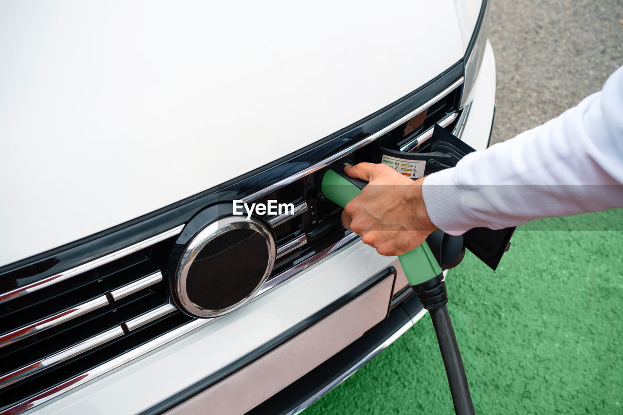 Man hand holding socket plugged into electric car