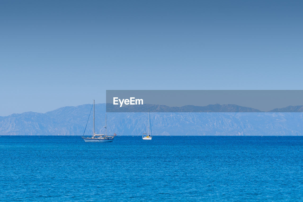 Tow sailing boats in ocean,in the background mountains.