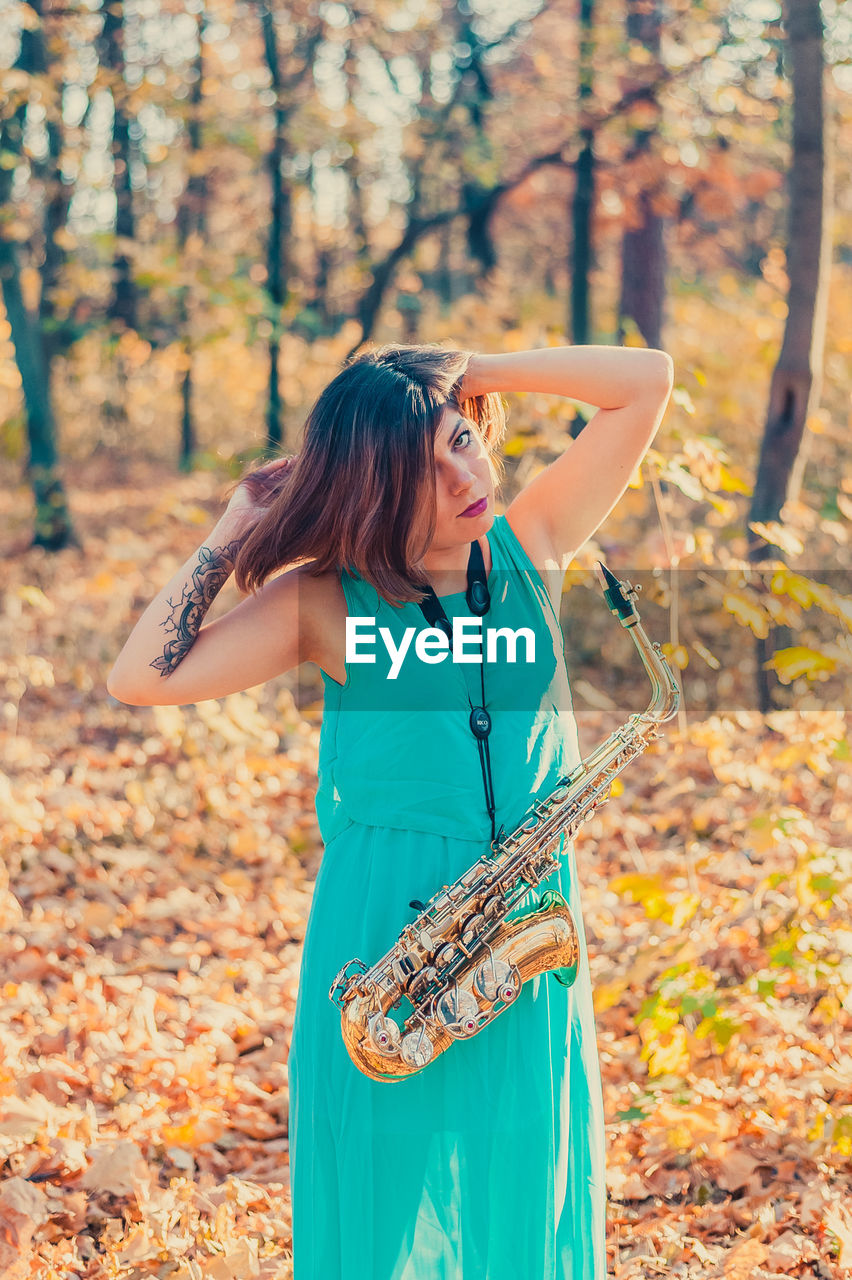 Woman with saxophone standing in forest during autumn