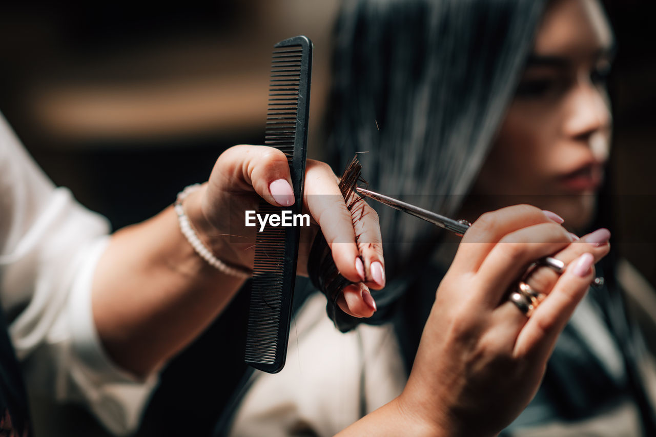 Cropped hands of hairdresser cutting woman hair in salon