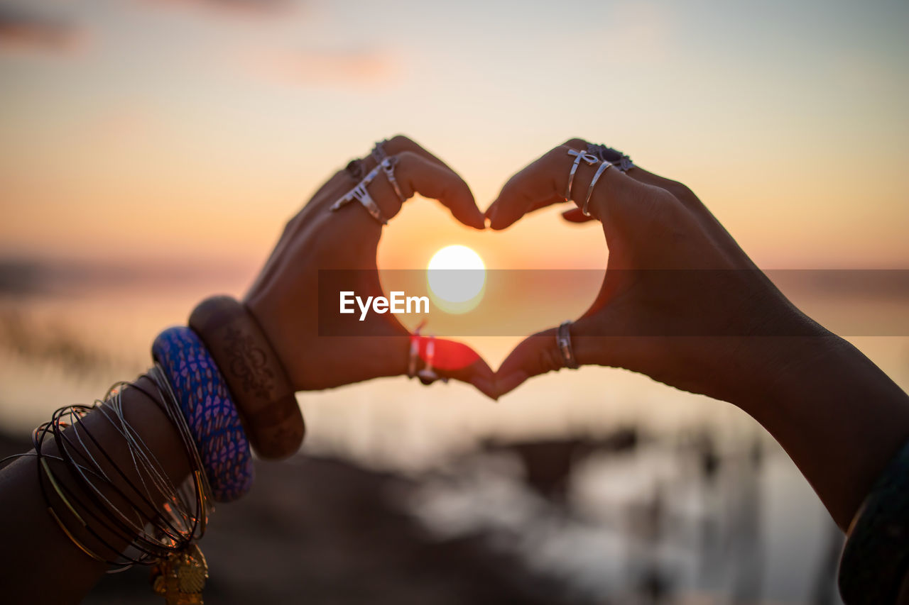 hand, love, positive emotion, heart shape, sunset, sky, emotion, adult, nature, focus on foreground, holding, romance, watch, togetherness, outdoors, women, sunlight, close-up, lifestyles, water, bracelet, dusk, bonding, valentine's day, beauty in nature, person, two people, silhouette, yellow