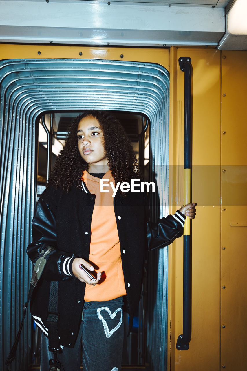 Teenage girl standing at doorway of tram while traveling during weekend