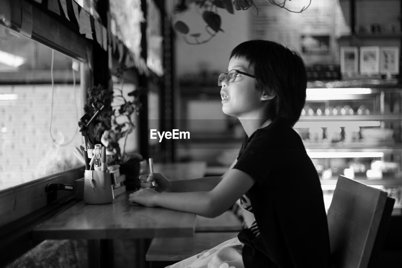 Side view of girl sitting at table by window