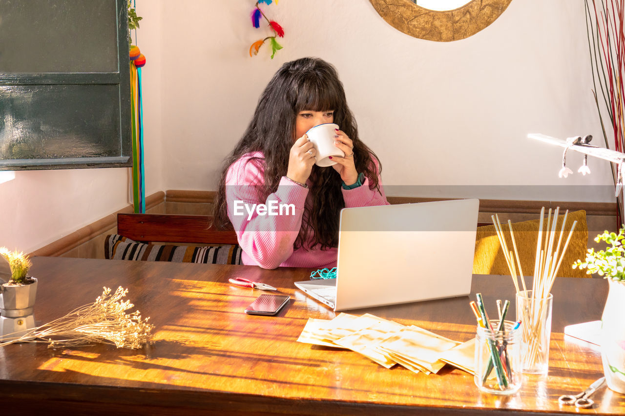 young woman using mobile phone while sitting on table