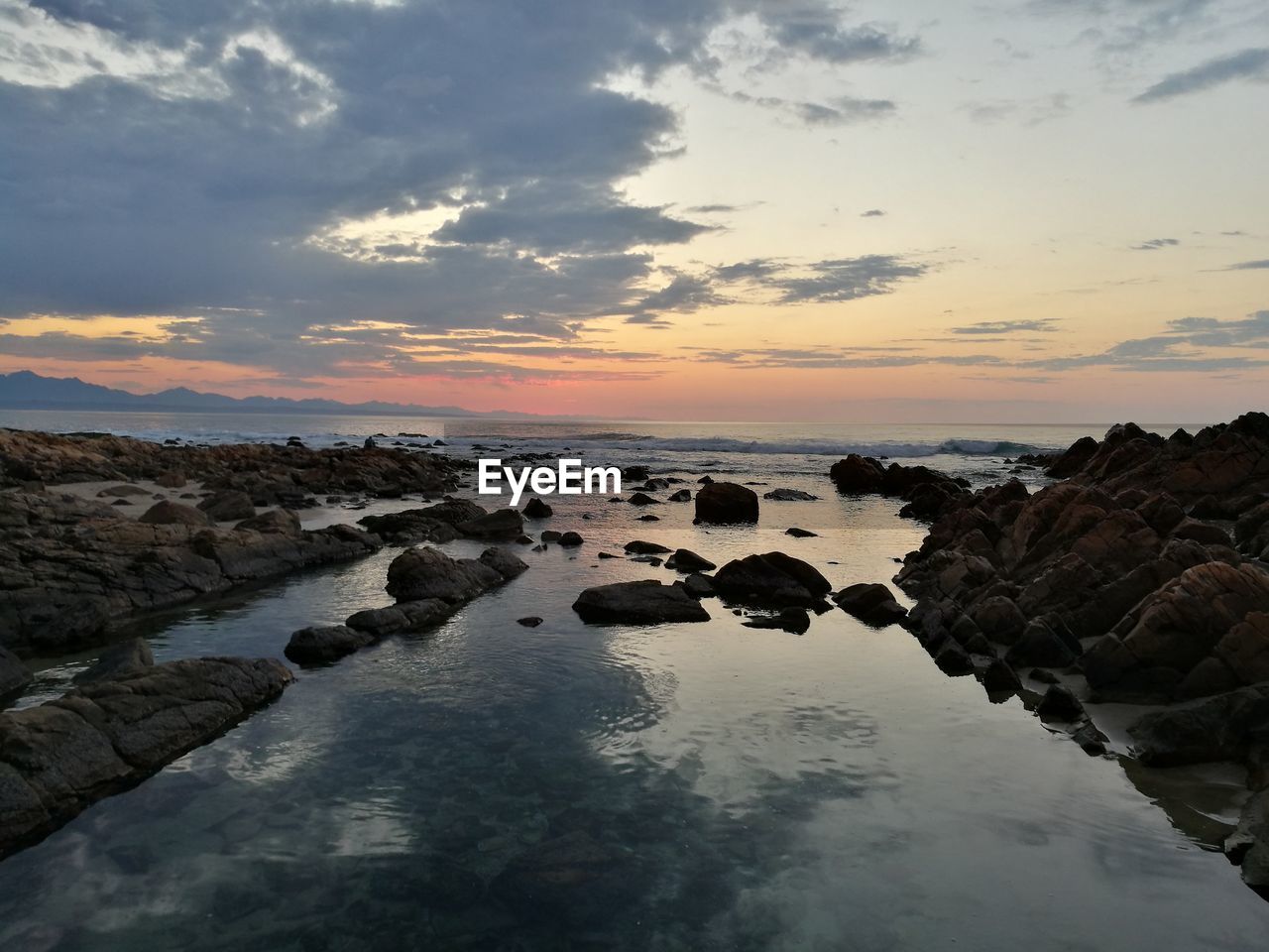 ROCKS IN SEA AGAINST SKY AT SUNSET